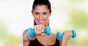 Brunette girl with blue dumbbells toning her muscles