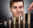 Young Businessman Stacking Coins At Desk